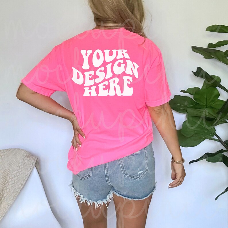May include: A bright pink t-shirt with the text "YOUR DESIGN HERE" in white, retro-style lettering on the back.
