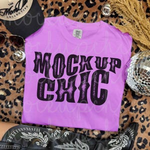 May include: A light purple t-shirt with the text "MOCK UP CHIC" in a black, decorative font. The shirt is displayed on a leopard print background, with a black hat and sunglasses visible.