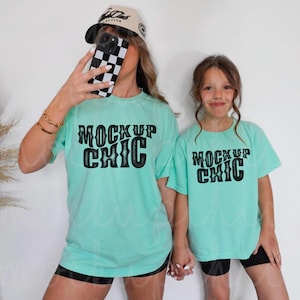 Puede incluir: Dos personas con camisetas a juego de color azul turquesa con el texto "Mock Up Chic" en negro. Las camisetas son de corte holgado y tienen un aspecto desgastado.