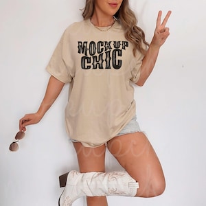 May include: A beige t-shirt with the text "MOCK UP CHIC" in black lettering. The shirt is being worn by a person with cowboy boots.