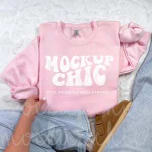 May include: A pink sweatshirt with the text "Mock Up Chic" in white, with the words "Real Models & Real Apparel" below. The sweatshirt is being modeled by a person wearing blue jeans.