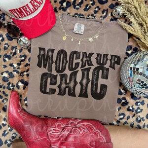 Puede incluir: Una camiseta color topo con las palabras "MOCKUP CHIC" en una fuente negra desgastada. La imagen también presenta una gorra de béisbol roja y blanca, gafas de sol, un collar dorado, una bola de discoteca y botas de vaquero rojas.
