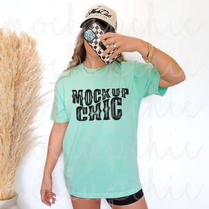 Może przedstawiać: Jasnozielony t-shirt z napisem "MOCK UP CHIC" czarnymi literami. Koszulkę nosi osoba w czarno-białej kratkowanej czapce z daszkiem.