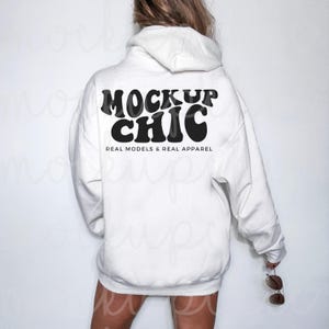May include: White hooded sweatshirt with the text "MOCKUP CHIC" in black retro-style lettering. The text is centered on the back of the sweatshirt. Below the text is the phrase "REAL MODELS & REAL APPAREL" in smaller black lettering.