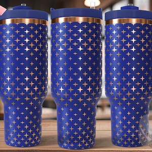 May include: Three stainless steel tumblers with a blue exterior and a copper-colored band around the top. The tumblers have a gold star pattern on the blue exterior. The tumblers have lids and handles.