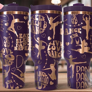 Pode incluir: Um copo de aço inoxidável roxo com um design dourado que apresenta dançarinos, corações e o texto "Keep Calm & Dance", "Eat Sleep Dance Repeat", "Live Love Dance" e "Dance Your Heart Out".