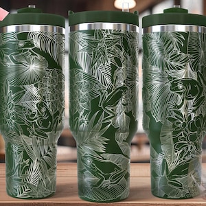 May include: Three green stainless steel tumblers with a white design of frogs and tropical leaves. The tumblers are seamless and have a lid and a handle.