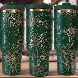 Puede incluir: Una taza de viaje verde con un diseño de hojas doradas. La taza tiene una tapa y un asa. La taza es sin costuras.