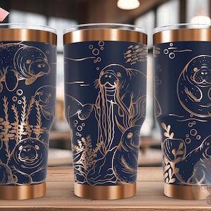 Puede incluir: Tres vasos de acero inoxidable con fondo azul marino y un diseño metálico dorado de manatíes y vida marina. Los vasos tienen una tapa y una base de color cobre.