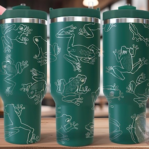 May include: A teal travel mug with a white outline frog pattern. The mug has a handle, a lid, and a silver rim. The text "SEAMLESS" is in a pink banner. The text "KTHOMP LASER DESIGNS" is in the lower right corner.
