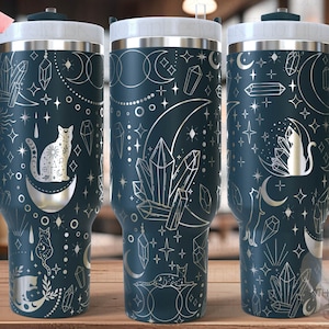 May include: Three stainless steel tumblers with a dark blue background and silver design. The design features moons, stars, crystals, and cats. The tumblers are seamless.