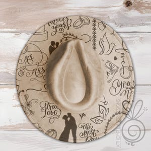 May include: Tan fedora hat with a decorative brim featuring wedding-themed illustrations and calligraphy. The brim displays silhouettes of a couple, rings, doves, and the phrases "Mr & Mrs", "True Love", and "You and Me".