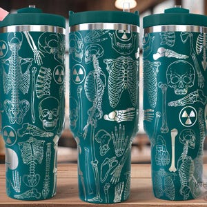 May include: Teal stainless steel travel mug with a white skeletal design. The mug has a handle and a lid. The design includes bones, skulls, and a radiation symbol.