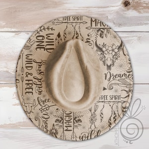 Può includere: Un cappello fedora beige con tesa larga, con un motivo decorativo di piume, un teschio di toro e le parole "Wild & Free", "Dreamer" e "Free Spirit" in carattere scritto a mano. Il cappello ha una corona a goccia.