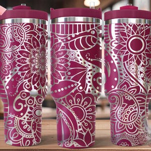 May include: A pink stainless steel tumbler with a silver mandala design. The tumbler has a lid and a handle. The word "SEAMLESS" is visible in the top left corner of the image.