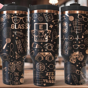 May include: A black and copper stainless steel travel mug with a handle. The mug is decorated with a gold eye chart and other eye-related graphics. The text on the mug reads "Keep It Glassy", "Bad puns are how I eye roll", "Eye You Prob", "One or Two", and "Our jokes don't get any cornea".