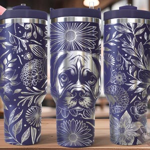 May include: A stainless steel tumbler with a navy blue background and a floral and pug design. The tumbler has a handle and a lid. The floral design is silver and includes flowers and leaves. The pug is in the center of the tumbler.