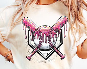 Op de afbeelding: Een wit T-shirt met een afbeelding van een honkbal, twee gekruiste knuppels en een honkplaat. De honkbal, knuppels en honkplaat zijn allemaal bedekt met roze glazuur en sprankjes.
