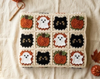 May include: A square crochet blanket featuring a grid of twelve motifs in cream, orange, white, and black. The design includes alternating squares of orange pumpkins with green stems, white ghosts with black eyes, and black cats with yellow eyes.