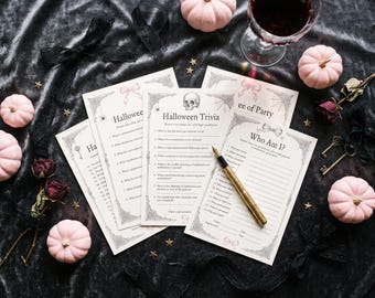 May include: A set of printed Halloween trivia and game cards featuring a skull illustration, spider webs, and bows. A gold-toned fountain pen rests on the Who Am I card. The cards include text such as Halloween Trivia and Who Am I.