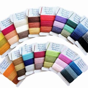 May include: A collection of colorful yarn skeins arranged in a fan shape. Each skein is labeled with text in a foreign language. The yarn colors range from vibrant reds and oranges to cool blues and greens, with neutral tones also present.