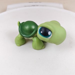 May include: A small green plastic turtle toy with a blue eye. The turtle has a green shell and is in a walking position.