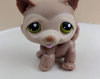 May include: A small brown and white plastic toy dog with green eyes and a pink tongue sticking out. The dog is sitting on a white surface.
