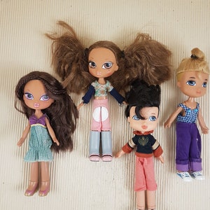 Könnte beinhalten: Vier Bratz-Puppen werden gezeigt, jede mit einzigartigen Frisuren und Outfits. Eine Puppe hat lange braune Haare und ein türkisfarbenes Kleid. Eine andere hat Zöpfe und ein rosa-blaues Outfit. Die dritte Puppe hat schwarze Haare und ein schwarz-oranges Oberteil. Die letzte Puppe hat blonde Haare und ein lila Outfit.