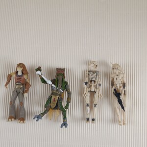 Op de afbeelding: Vier actionfiguren uit het Star Wars universum. De figuren zijn gemaakt van plastic en zijn geschilderd in verschillende kleuren, waaronder bruin, groen en wit. De figuren staan in verschillende actiehoudings.