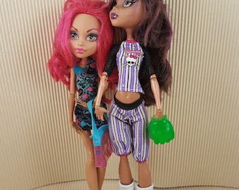 May include: Two Monster High dolls, one with pink hair and a blue and black outfit, the other with purple hair and a purple and white striped outfit, holding a green ball.