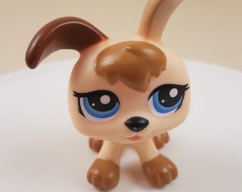May include: A small, cream-colored toy dog with brown ears and a brown patch on its head. The dog has blue eyes and a black nose.