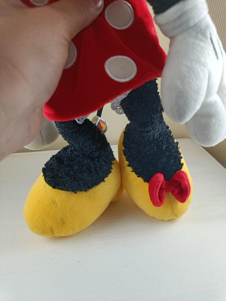 May include: A red and white polka dot dress with a white lace trim and yellow shoes with a red bow. The shoes are on a white surface.