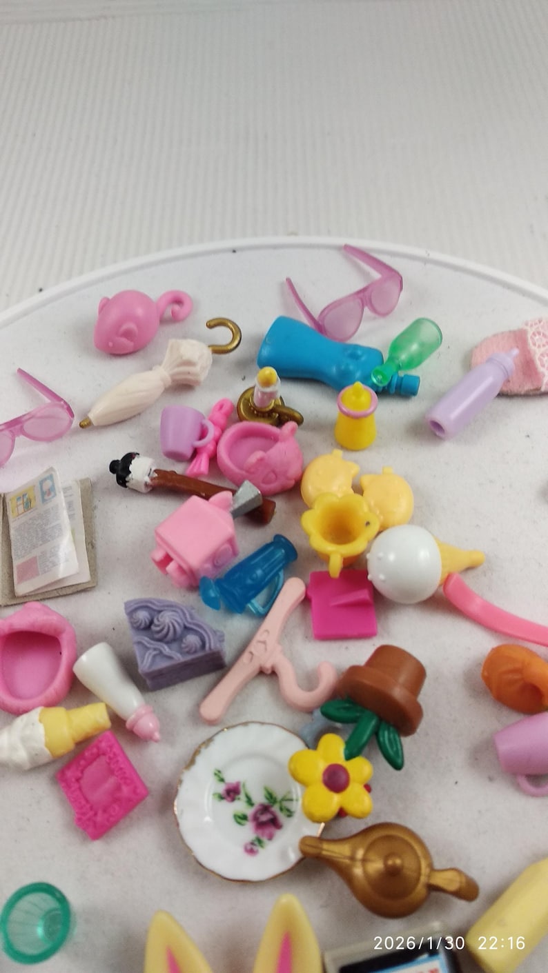 Puede incluir: Una colecci&oacute;n de accesorios de casa de mu&ntilde;ecas en miniatura en varios colores. Incluye peque&ntilde;as gafas de sol, botellas, un plato con dise&ntilde;o floral, una tetera y otros juguetes peque&ntilde;os. Los art&iacute;culos est&aacute;n dispersos sobre una superficie blanca.