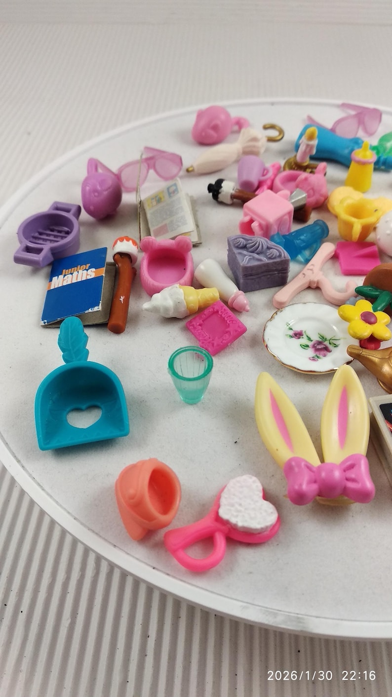 Puede incluir: Una colecci&oacute;n de accesorios en miniatura para casas de mu&ntilde;ecas en varios colores, que incluyen una cuchara azul con un recorte en forma de coraz&oacute;n, un cepillo para el pelo rosa y orejas de conejo amarillas con un lazo rosa. Otros art&iacute;culos incluyen un plato con un dise&ntilde;o floral y un libro en miniatura.