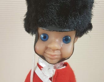 Könnte beinhalten: Eine Spielzeugsoldatenpuppe, die eine rote Uniform mit weißen Verzierungen und einen schwarzen Pelzhut trägt. Die Puppe hat blaue Augen und ein lächelndes Gesicht.