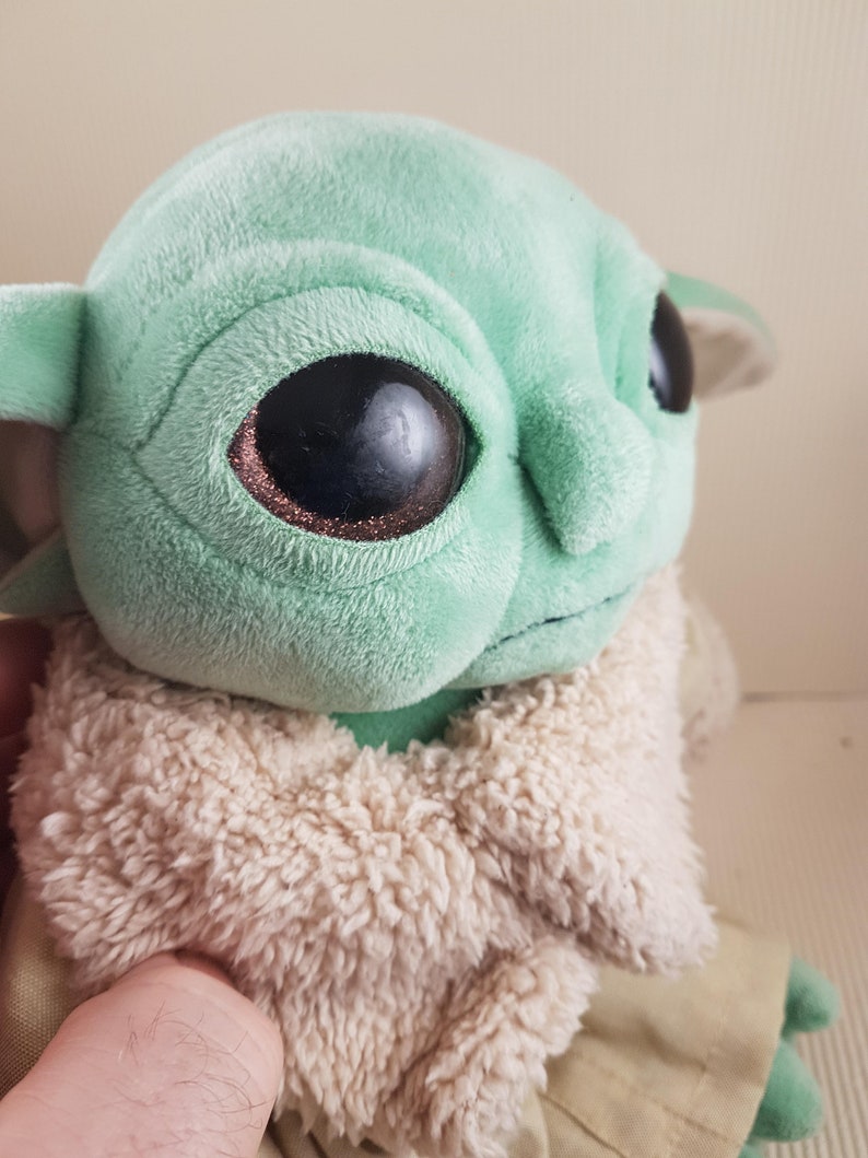 May include: A green plush toy with large black eyes and a brown fur coat. The toy is a popular character from the Star Wars franchise.