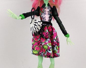 May include: A green and pink Monster High doll with long pink and green hair, wearing a black and white patterned dress, a black jacket, and gold boots. She is holding a black and white purse.