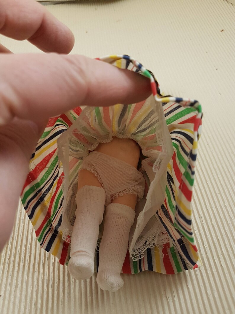 May include: A doll wearing a white dress with a colorful striped skirt and white socks.