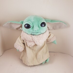 May include: A green plush toy with large brown eyes and a tan coat. The toy is a character from the Star Wars franchise.