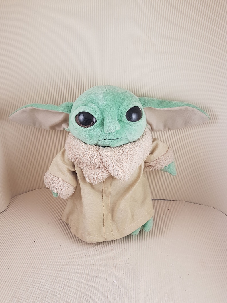 May include: A green plush toy with large brown eyes and a tan coat. The toy is a character from the Star Wars franchise.