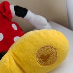 May include: Yellow plush Mickey Mouse glove with a gold Disney Theme Parks Authentic Original tag.