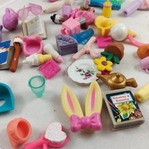 Puede incluir: Una colecci&oacute;n de juguetes en miniatura de varios colores, incluyendo rosa, amarillo, azul y blanco. Los juguetes incluyen una diadema de orejas de conejo, un peque&ntilde;o libro con el texto "Painting & Drawing", un plato y otros objetos peque&ntilde;os.