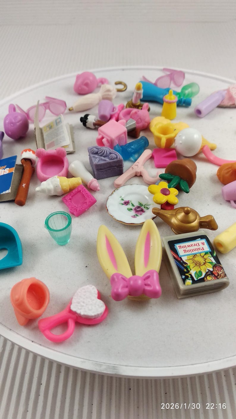 Puede incluir: Una colecci&oacute;n de juguetes en miniatura de varios colores, incluyendo rosa, amarillo, azul y blanco. Los juguetes incluyen una diadema de orejas de conejo, un peque&ntilde;o libro con el texto "Painting & Drawing", un plato y otros objetos peque&ntilde;os.