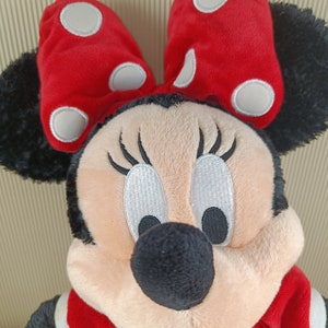 May include: A plush toy of Minnie Mouse wearing a red dress with white polka dots and a red bow with white polka dots. She has black ears, a black nose, and black eyes with white eyelashes.