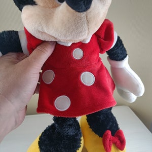 May include: A plush Minnie Mouse toy wearing a red dress with white polka dots and yellow shoes with red bows.