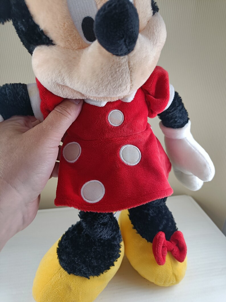 May include: A plush Minnie Mouse toy wearing a red dress with white polka dots and yellow shoes with red bows.