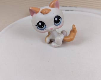 May include: A white and orange cat figurine with blue eyes. The cat is sitting with its tail curled around its legs.