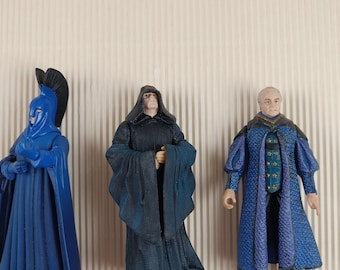 May include: Three action figures of characters from the Star Wars universe. The figures are dressed in robes and are standing on a textured background.