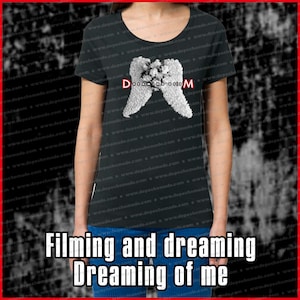 May include: Black t-shirt with a white graphic of angel wings and the text "Dreaming of Me". The text is in a bold, white font. The t-shirt is a women's style with a scoop neck.