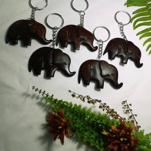 May include: Five brown coconut shell elephant keychains with silver key rings. The keychains are arranged in a semi-circle on a white surface.